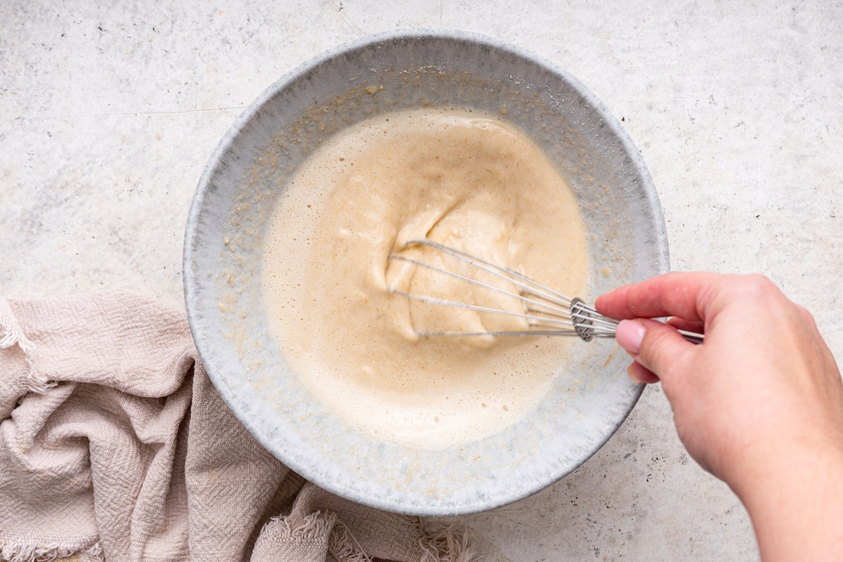 A woman's hand uses a metal whisk to create a protein pancake batter.