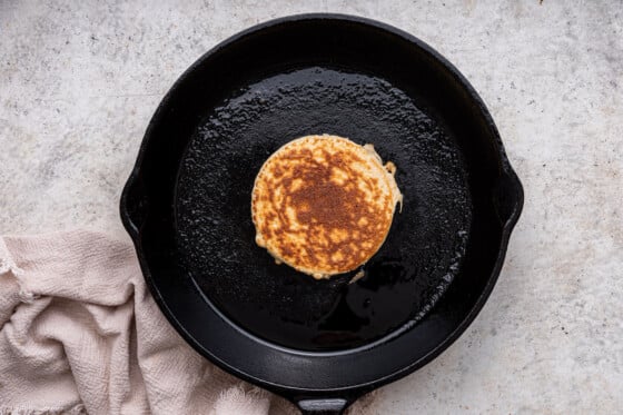 A protein pancake with a golden crisp finish in a cast iron skillet.