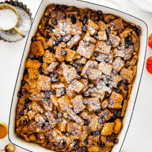 Pumpkin French Toast Casserole in a square baking dish topped with powdered sugar and chocolate chips.