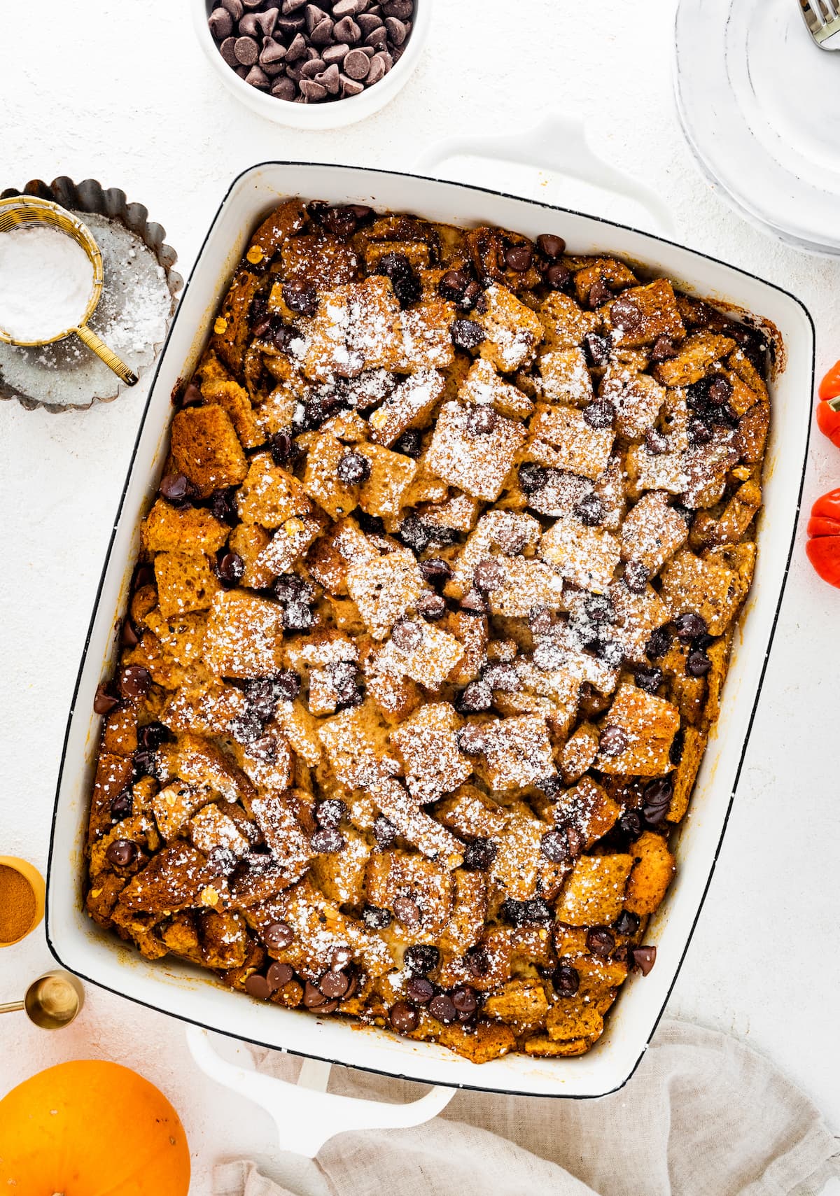 Pumpkin French Toast Casserole in a square baking dish topped with powdered sugar and chocolate chips.