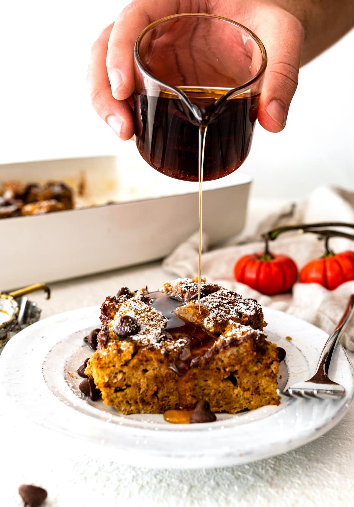 Maple syrup being poured over a piece of Pumpkin French Toast Casserole on a small plate.