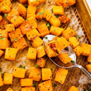 Seasoned and cubed roasted butternut squash on a baking tray with a metal spoon.