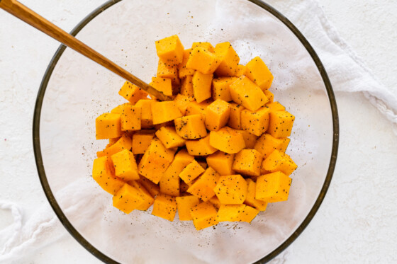 Seasoning added to cubed butternut squash in a large glass bowl.