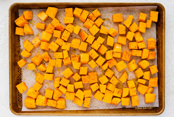 Seasoned and cubed butternut squash on a baking tray before being roasted.