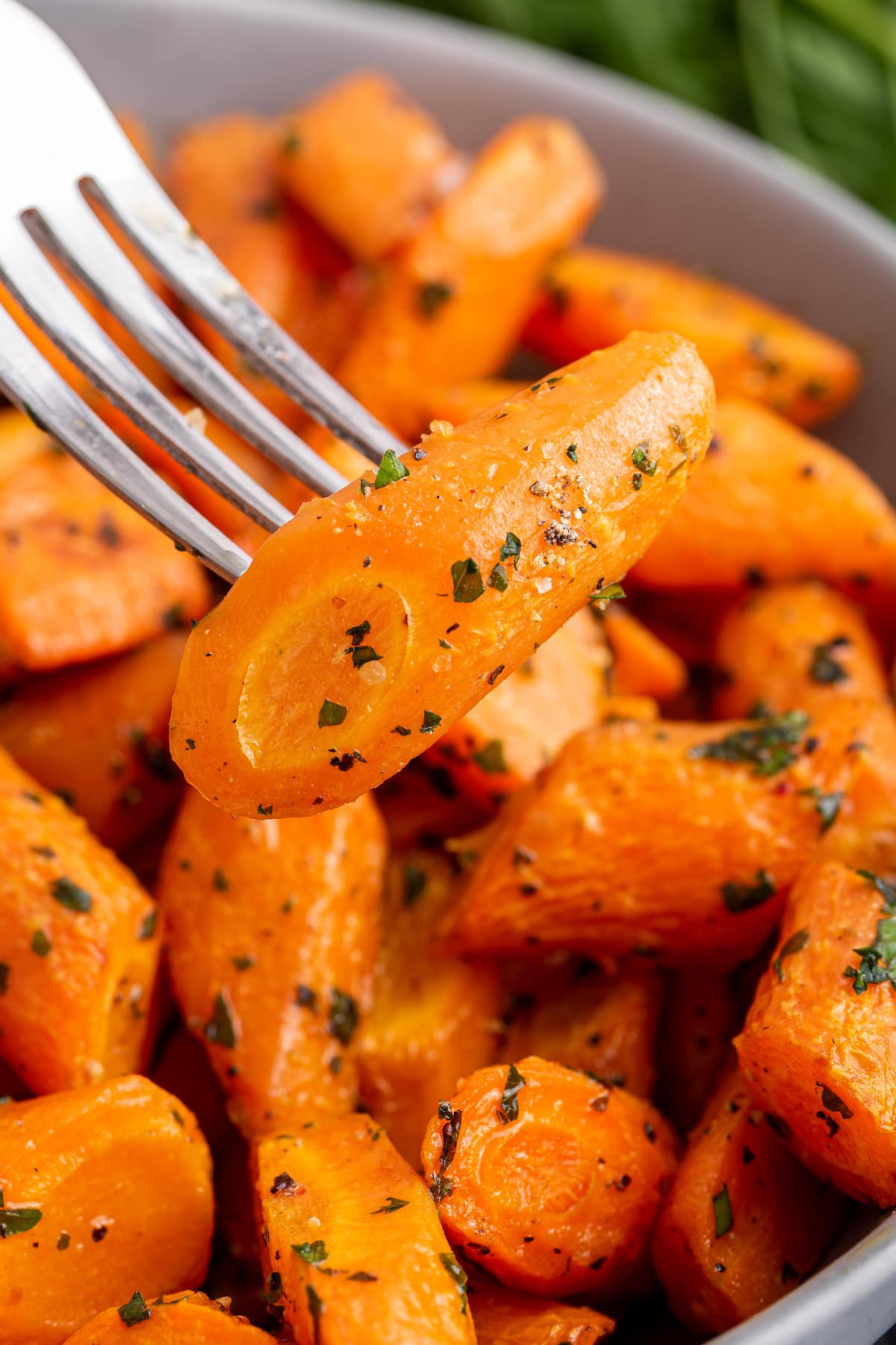 A fork holding a roasted carrot over a bowl of other roasted carrots.