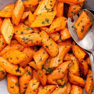 Roasted carrots in a bowl with two metal serving spoons.