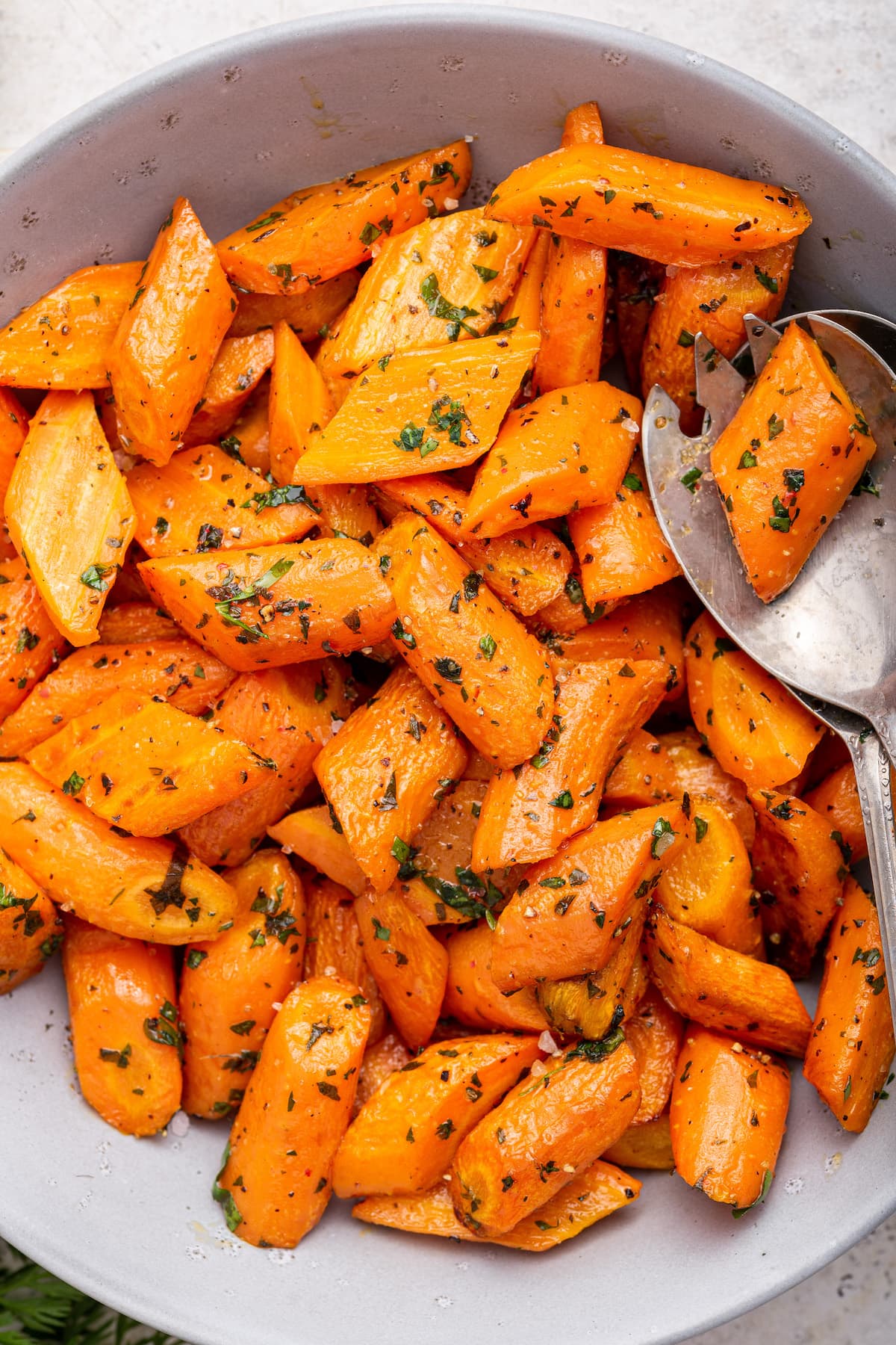 Roasted carrots in a bowl with two metal serving spoons.