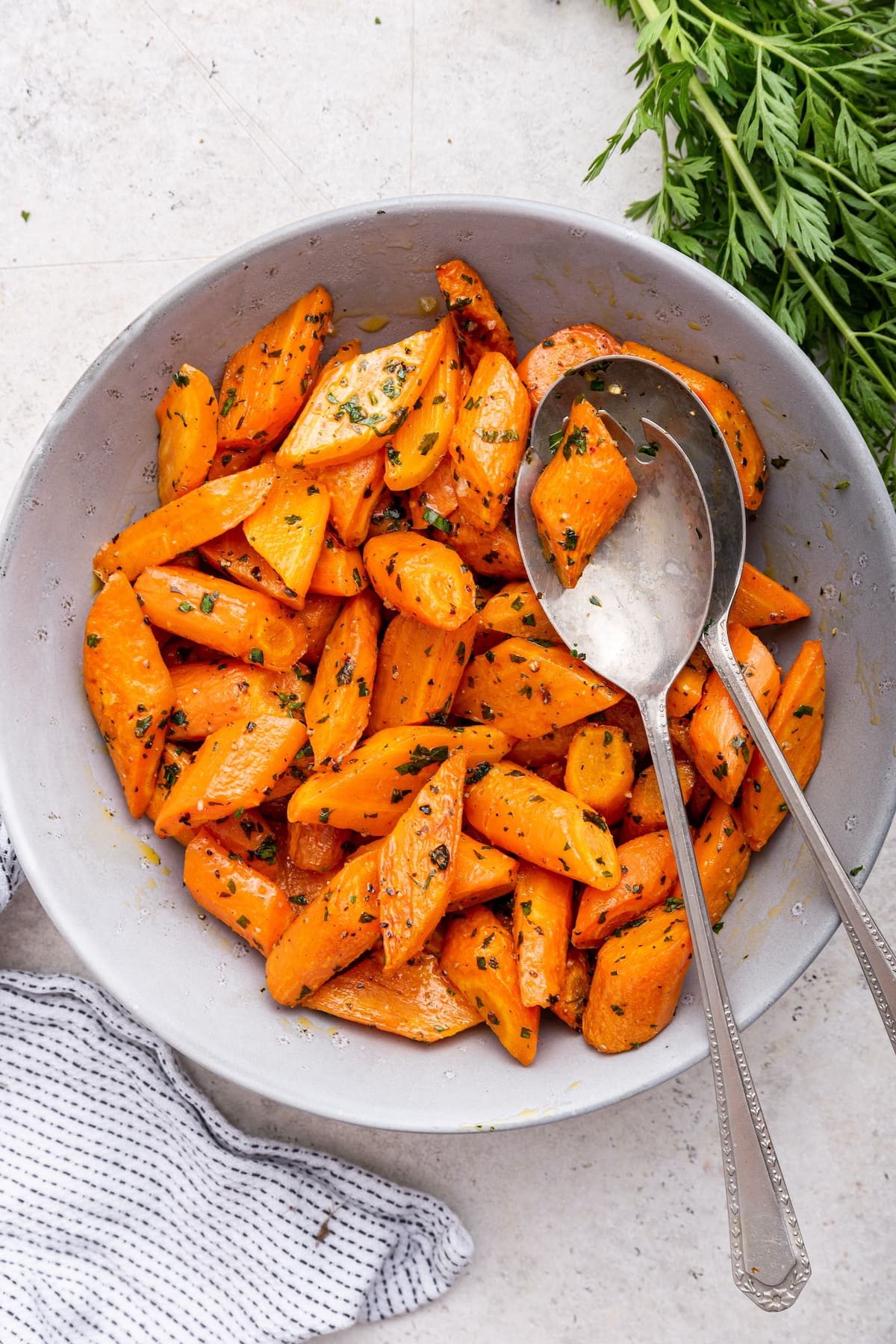 Roasted carrots in a bowl with two metal serving spoons.