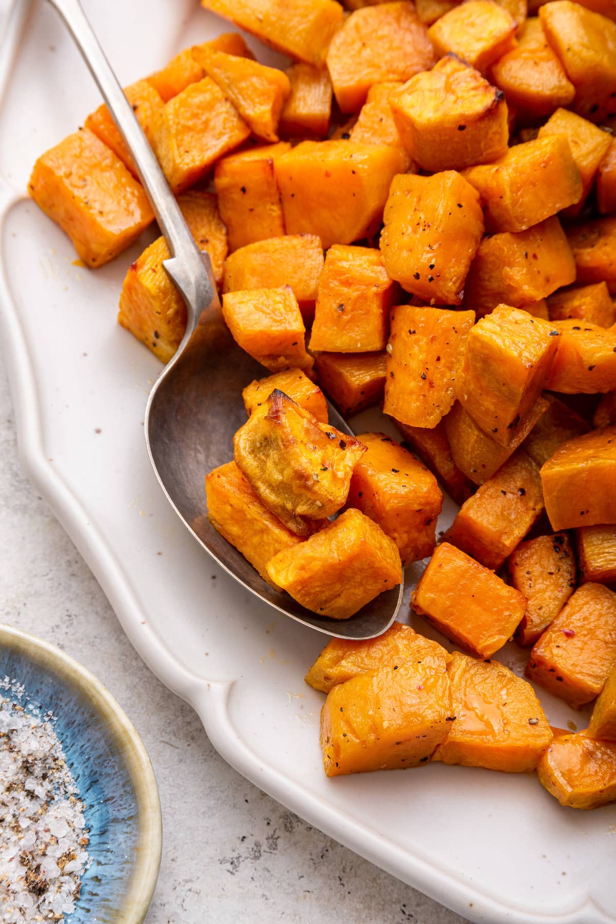 Cubed roasted sweet potatoes on a plate with a metal spoon holding a few of them.