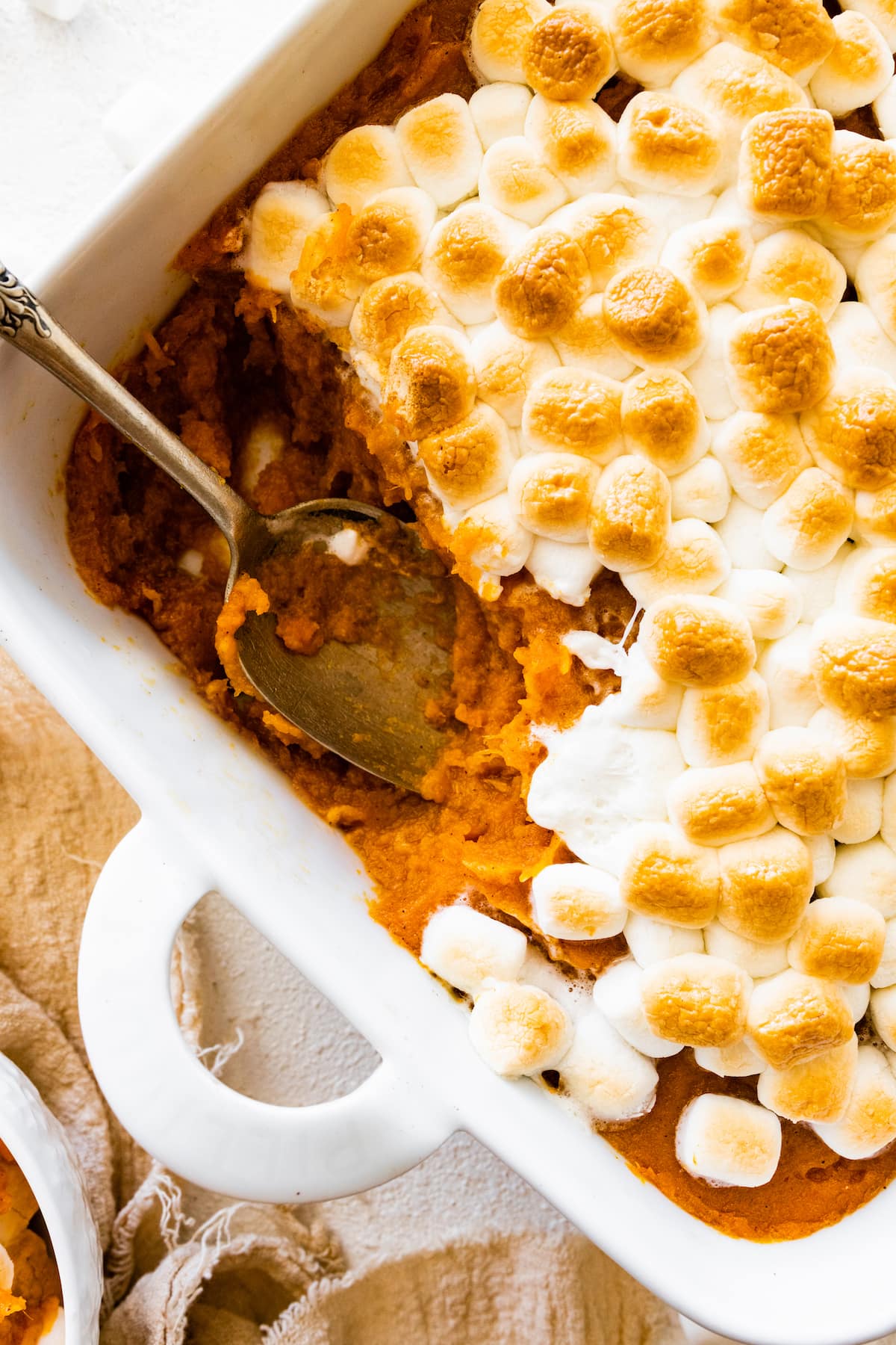 Sweet potato casserole in a square baking dish with a portion missing in the corner where a metal spoon is.