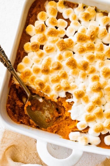 Sweet potato casserole in a square baking dish with a portion missing in the corner where a metal spoon is.