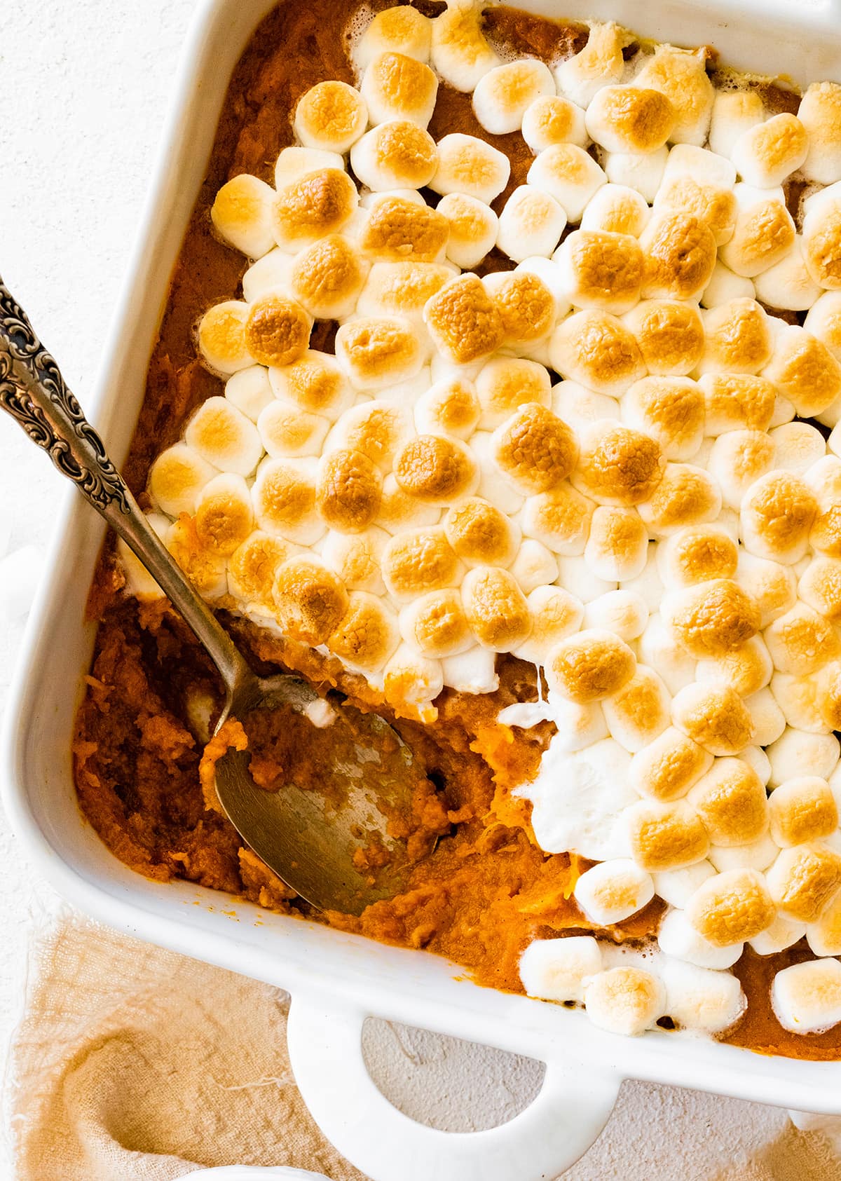 Sweet potato casserole in a square baking dish with a portion missing in the corner where a metal spoon is.