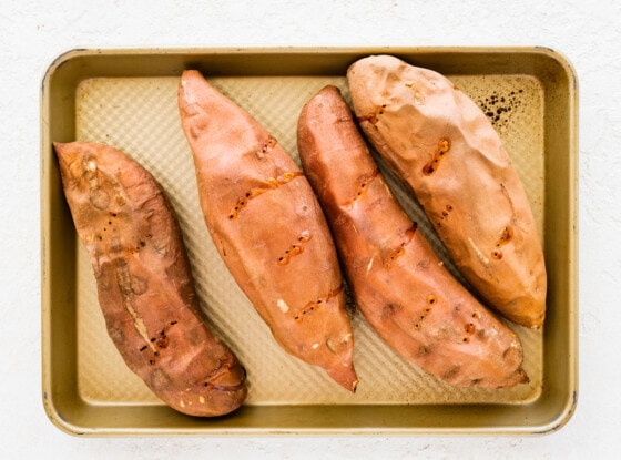 Four large sweet potatoes on a baking tray.