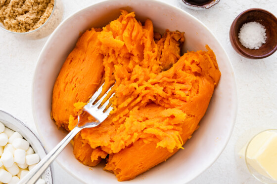 A fork is used to mash sweet potatoes in a large bowl.