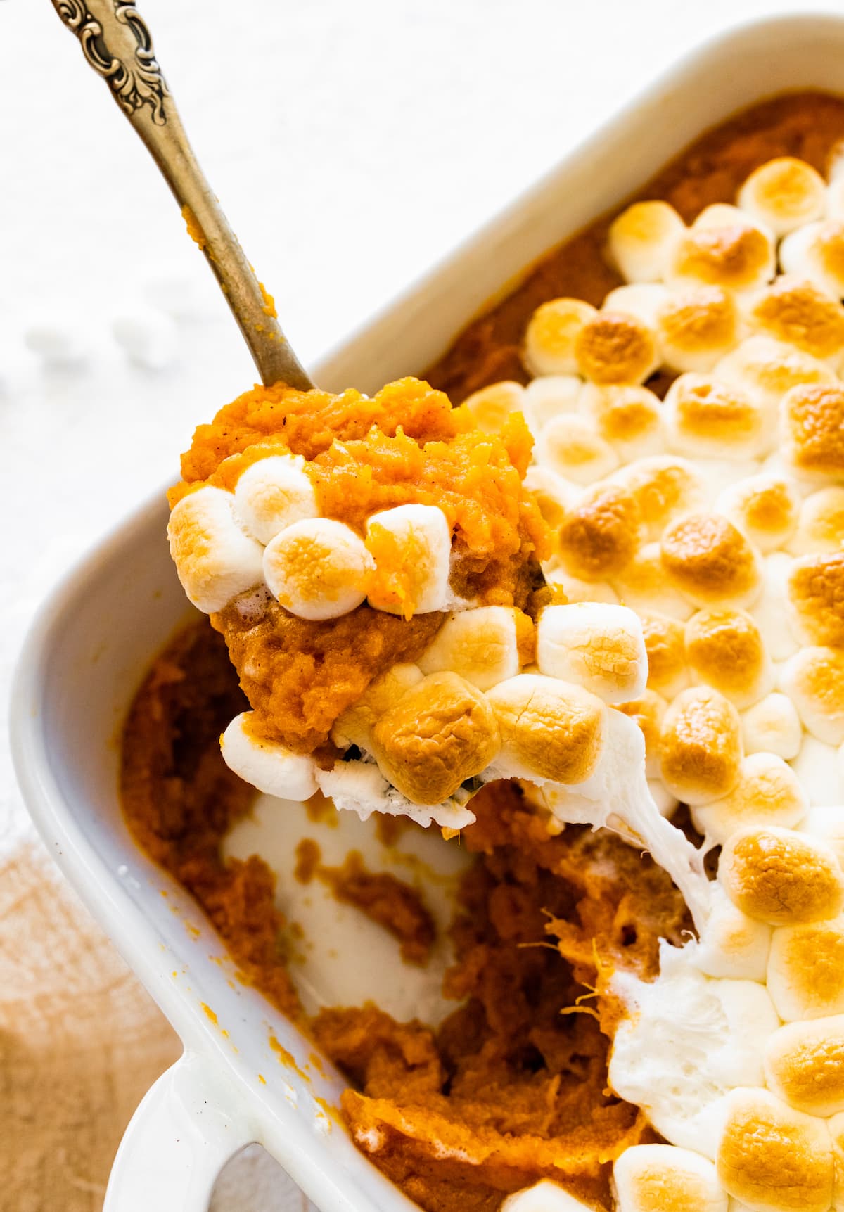 A spoon taking a small portion of sweet potato casserole from a square baking dish.