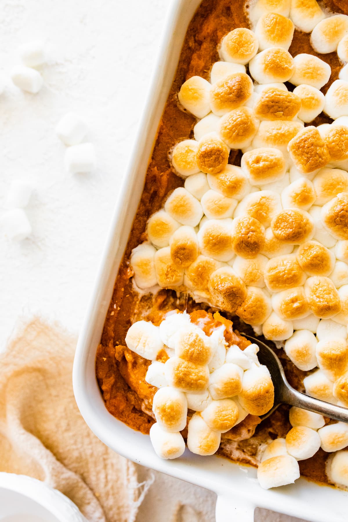 Sweet potato casserole in a square baking dish with a metal spoon removing some of the casserole.