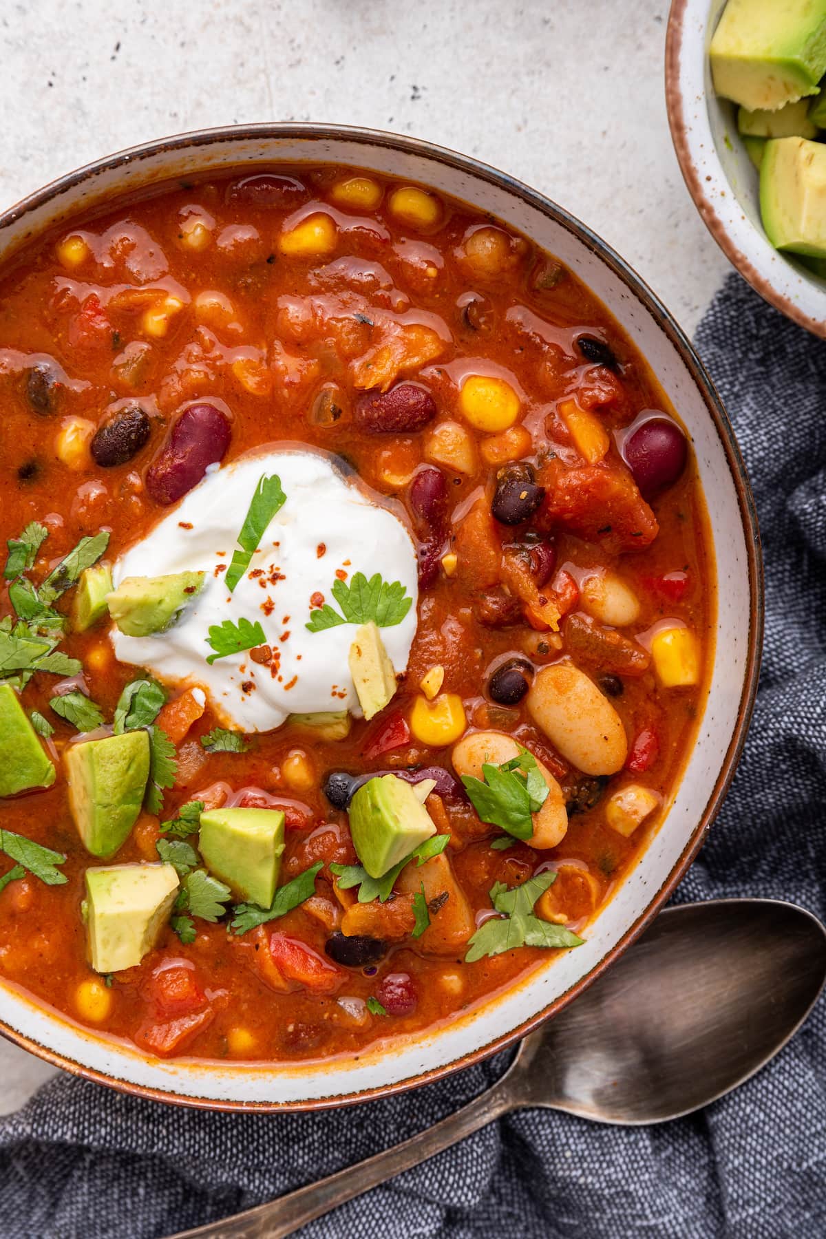 Vegetarian chili in a bowl. The chili is garnished with cilantro, sour cream, and avocado.