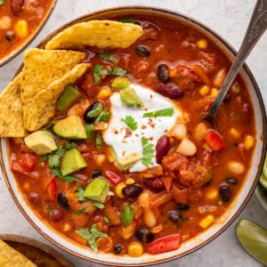 Vegetarian chili in a bowl with tortilla chips and a spoon. The chili is garnished with cilantro, sour cream, and avocado.