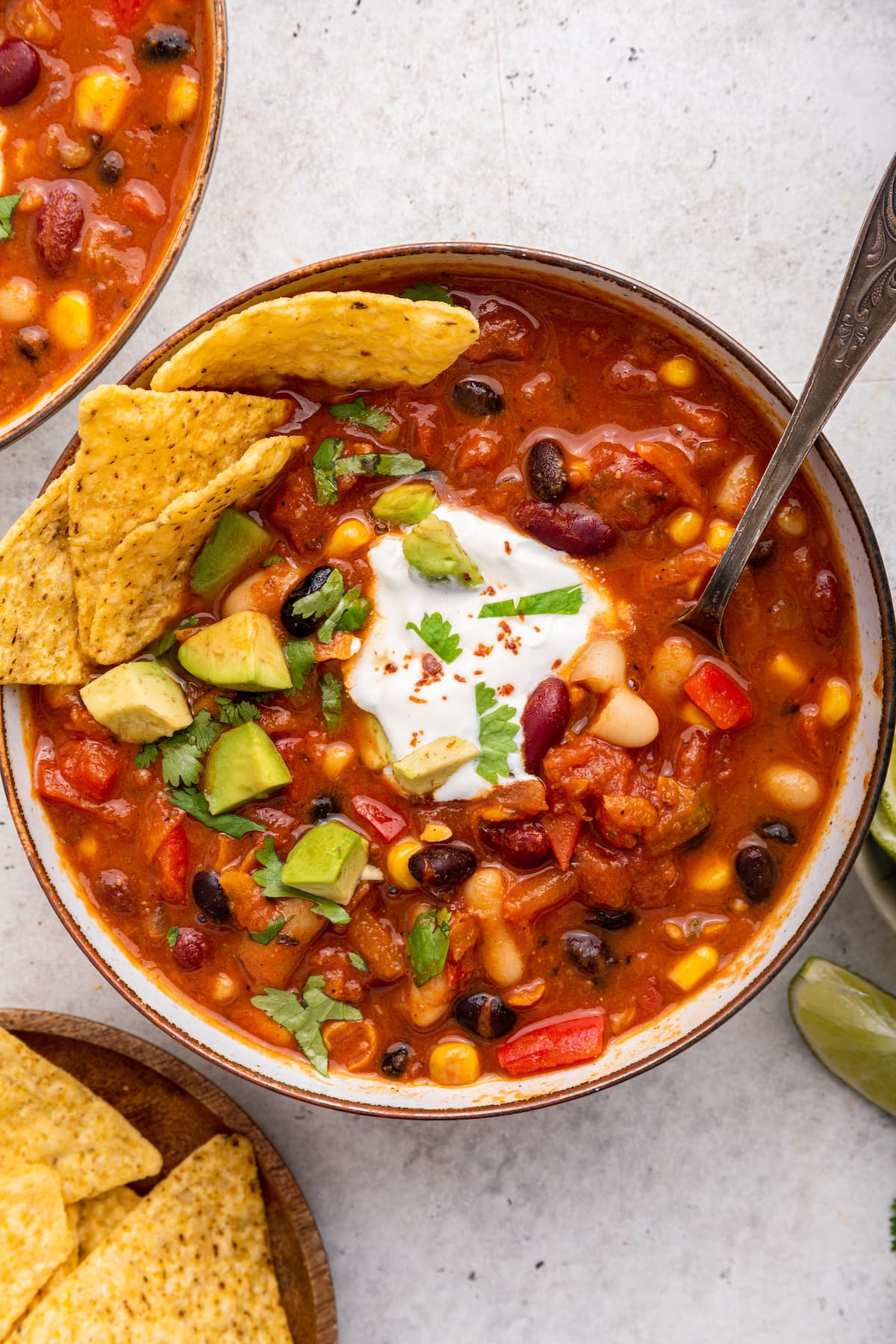 Vegetarian chili in a bowl with tortilla chips and a spoon. The chili is garnished with cilantro, sour cream, and avocado.