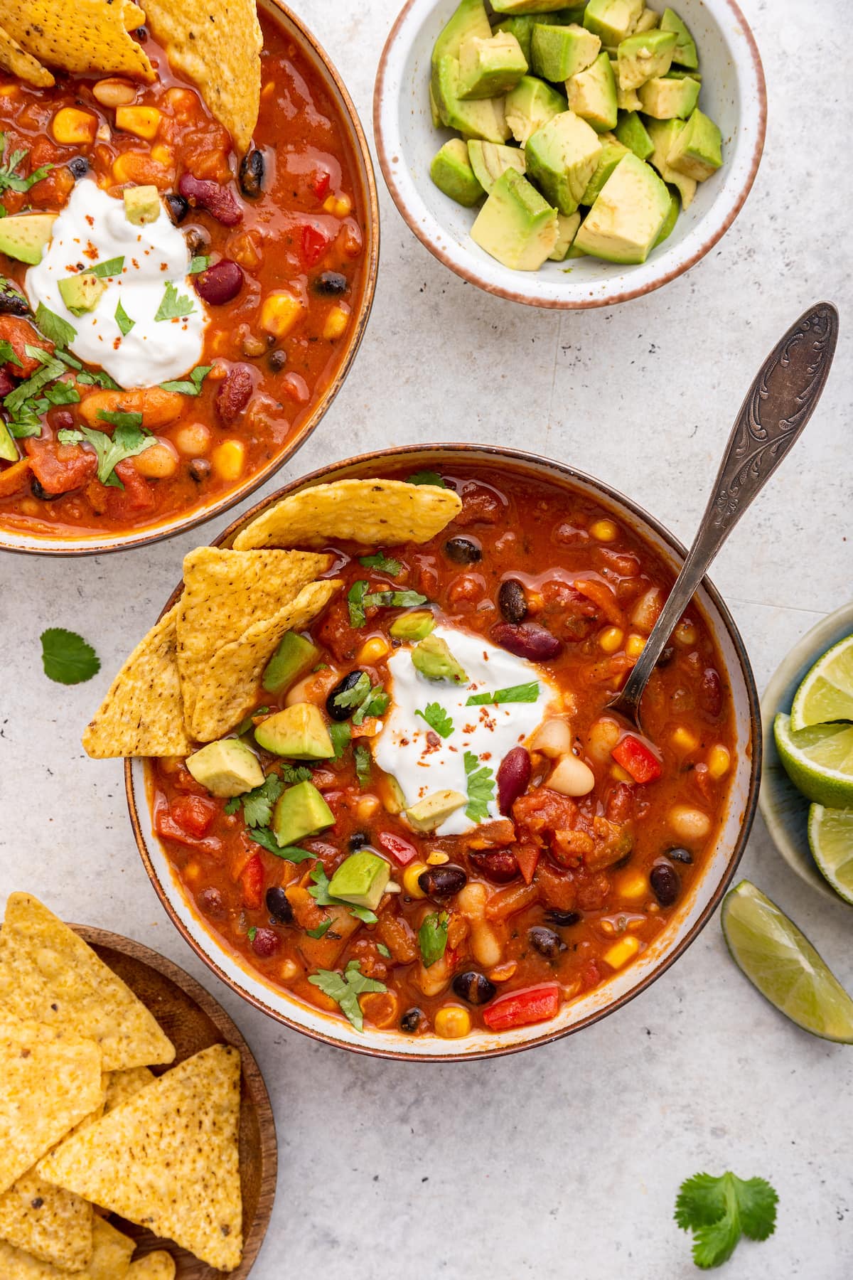 Vegetarian chili in a bowl with tortilla chips and a spoon. The chili is garnished with cilantro, sour cream, and avocado.