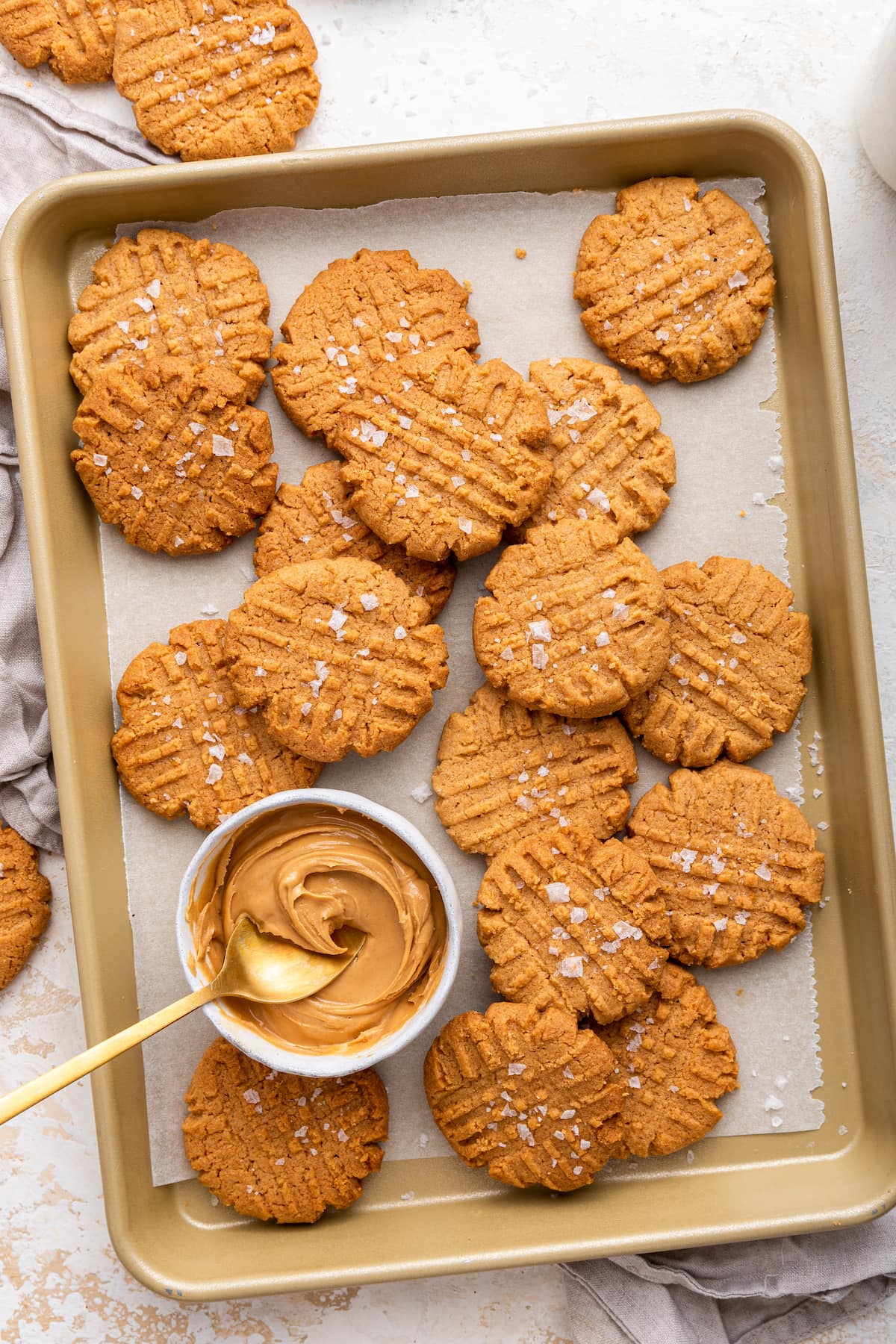 Peanut butter cookies on a baking sheet with a bowl of peanut butter.