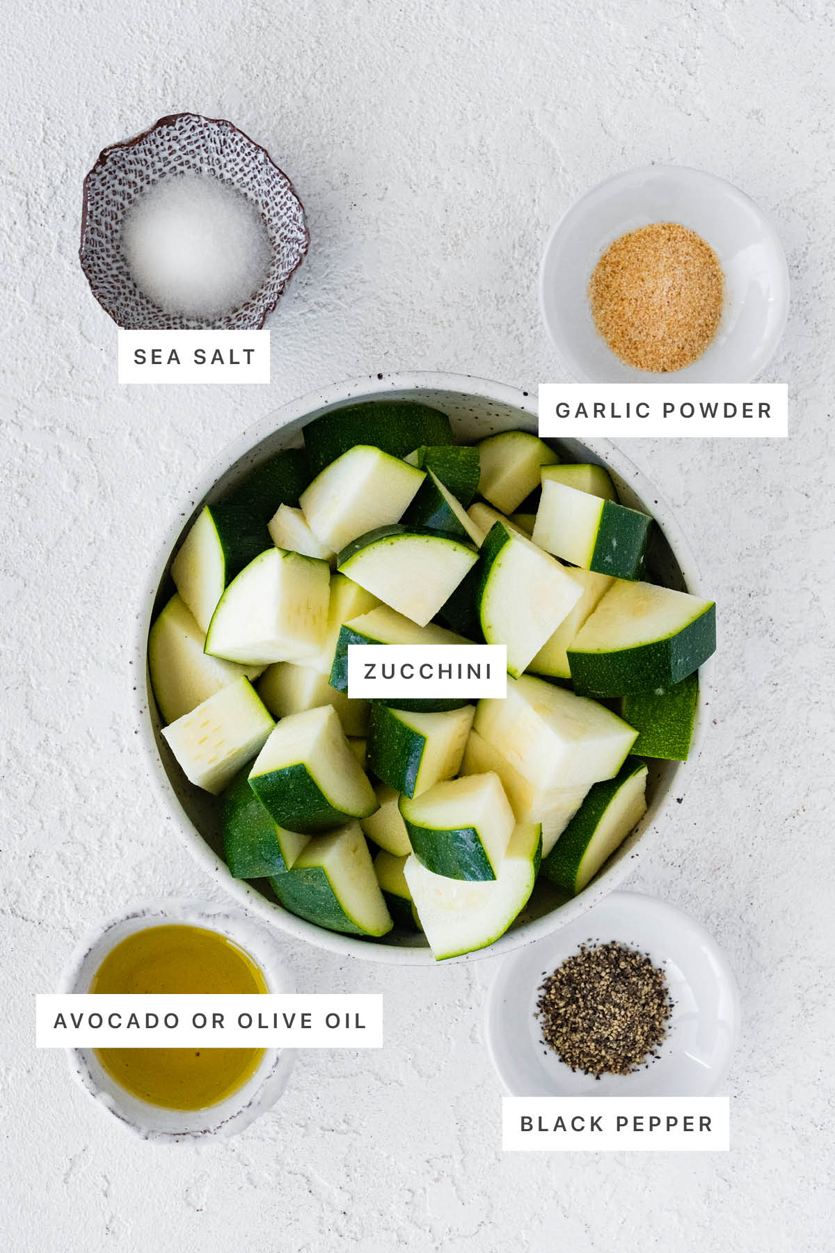 Ingredients measured out for ​Air Fryer Zucchini: sea salt, garlic powder, zucchini, olive oil and black pepper.