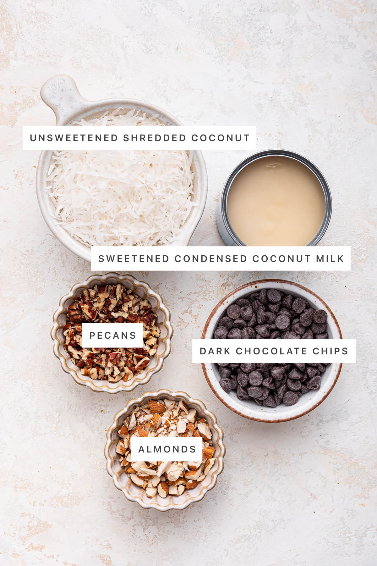 Ingredients measured out to make 5-Ingredient Chocolate Coconut Bars: unsweetened shredded coconut, sweetened condensed coconut milk, pecans, dark chocolate chips and almonds.