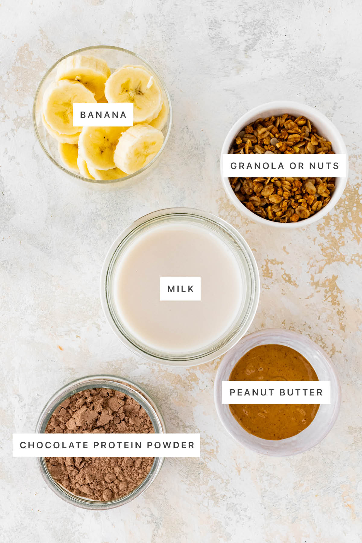 Ingredients measured out to make Chocolate Peanut Butter Ninja Creami Protein Ice Cream: banana, granola or nuts, milk, peanut butter and chocolate protein powder.