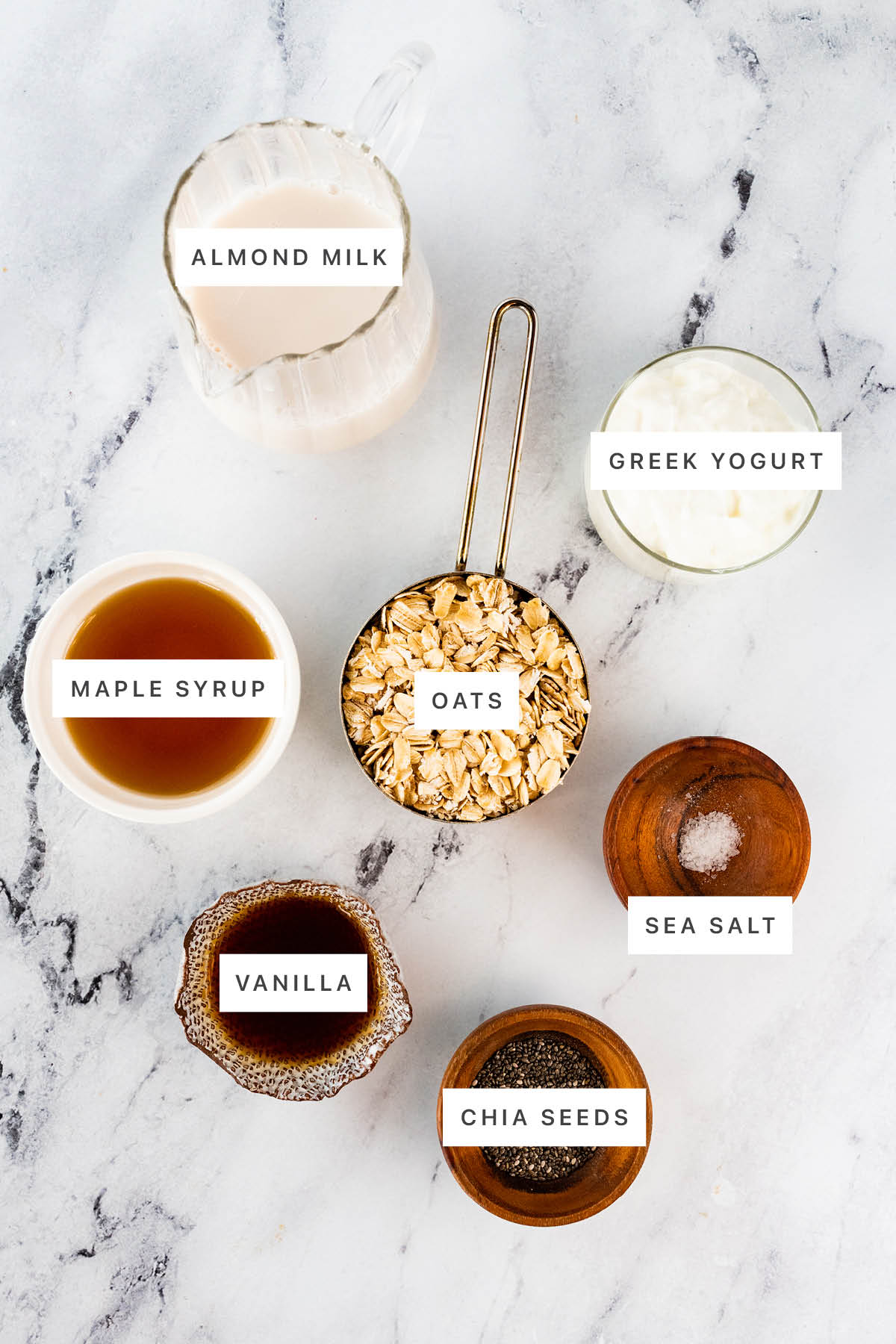 Ingredients measured out to make overnight oats: almond milk, Greek yogurt, maple syrup, oats, sea salt, vanilla and chia seeds.