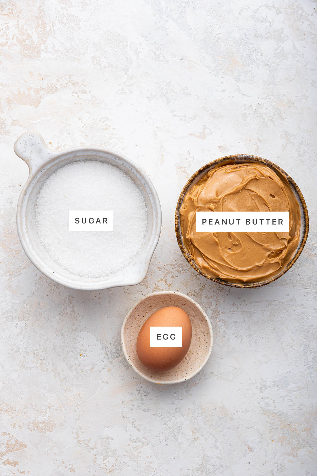 Ingredients measured out to make 3 Ingredient Peanut Butter Cookies: sugar, peanut butter and egg.