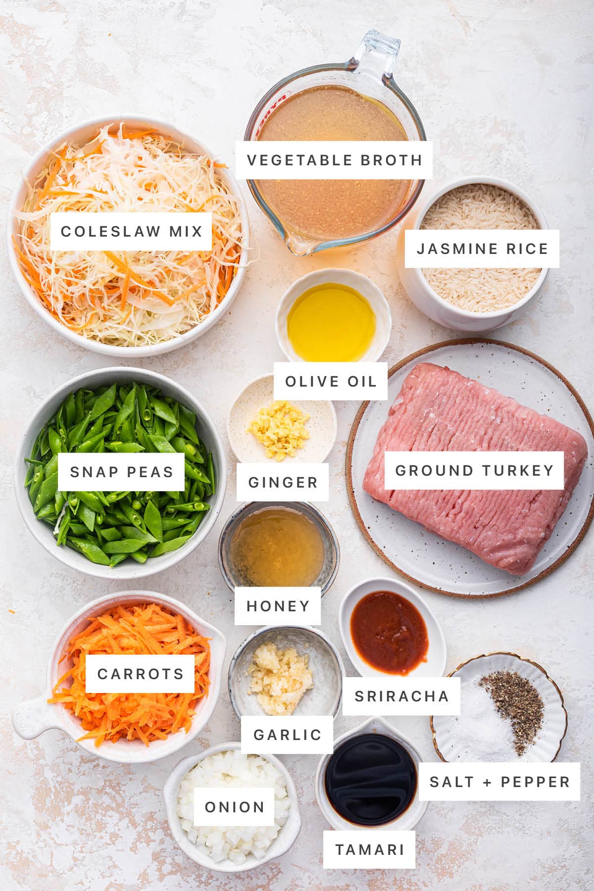 Ingredients measured out to make Tamari Ground Turkey Skillet: coleslaw mix, vegetable broth, jasmine rice, olive oil, ginger, ground turkey, snap peas, honey, sriracha, carrots, garlic, onion, tamari, salt and pepper.