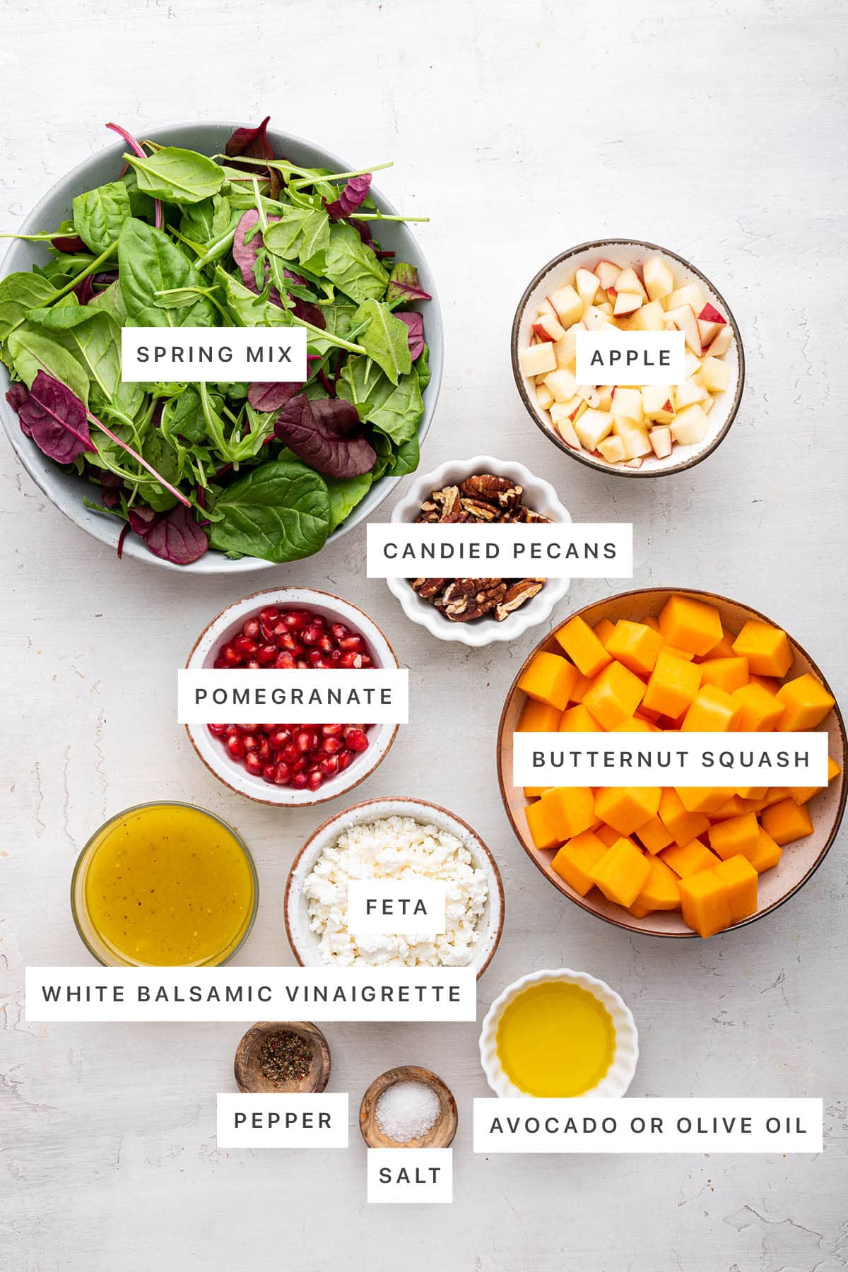 Ingredients measured out to make a Winter Salad: spring mix, candied pecans, apple, pomegranate, butternut squash, white balsamic vinaigrette, feta, pepper, salt and olive oil.