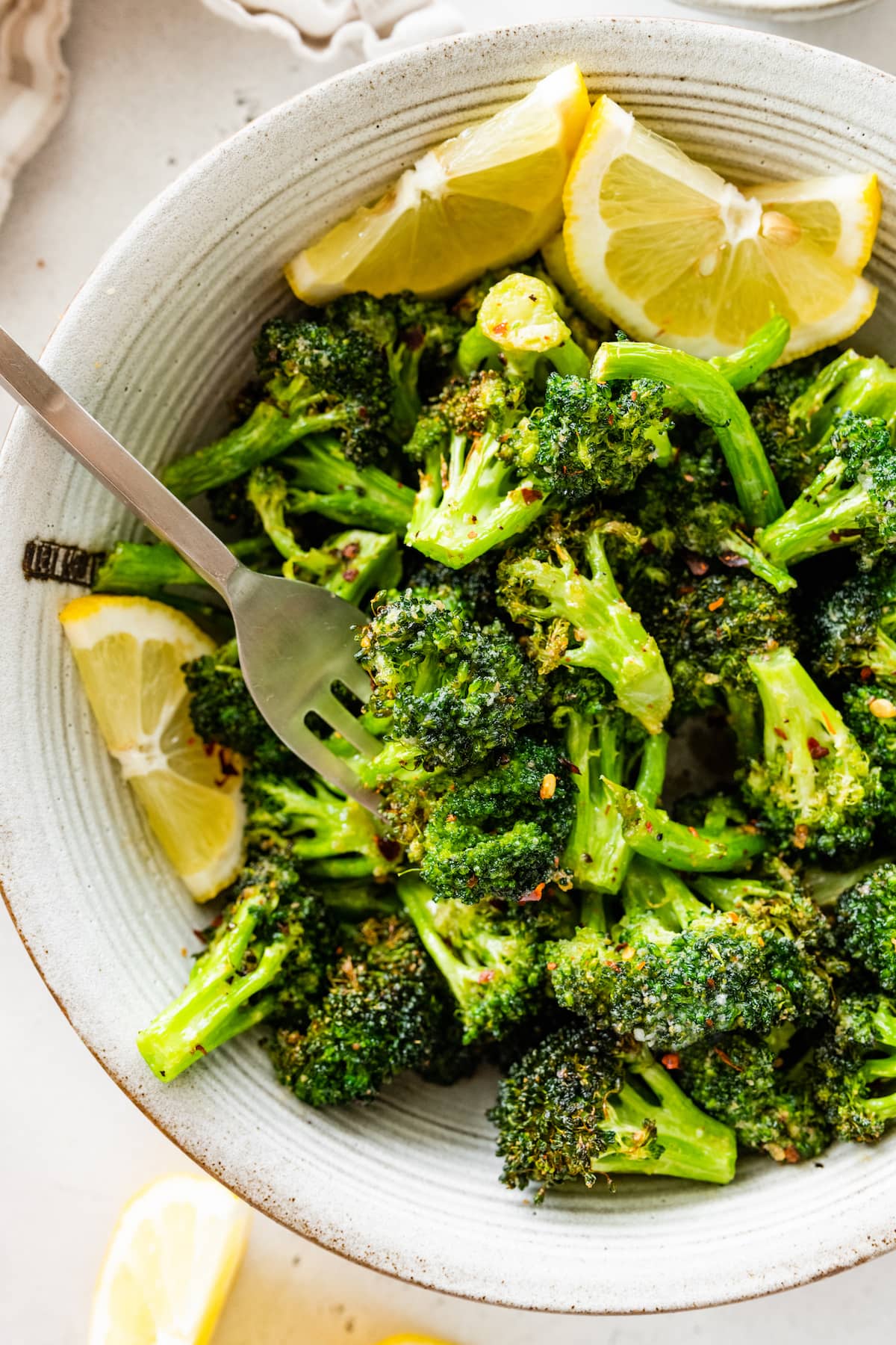 Seasoned air-fried broccoli in a large bowl with lemon wedges.