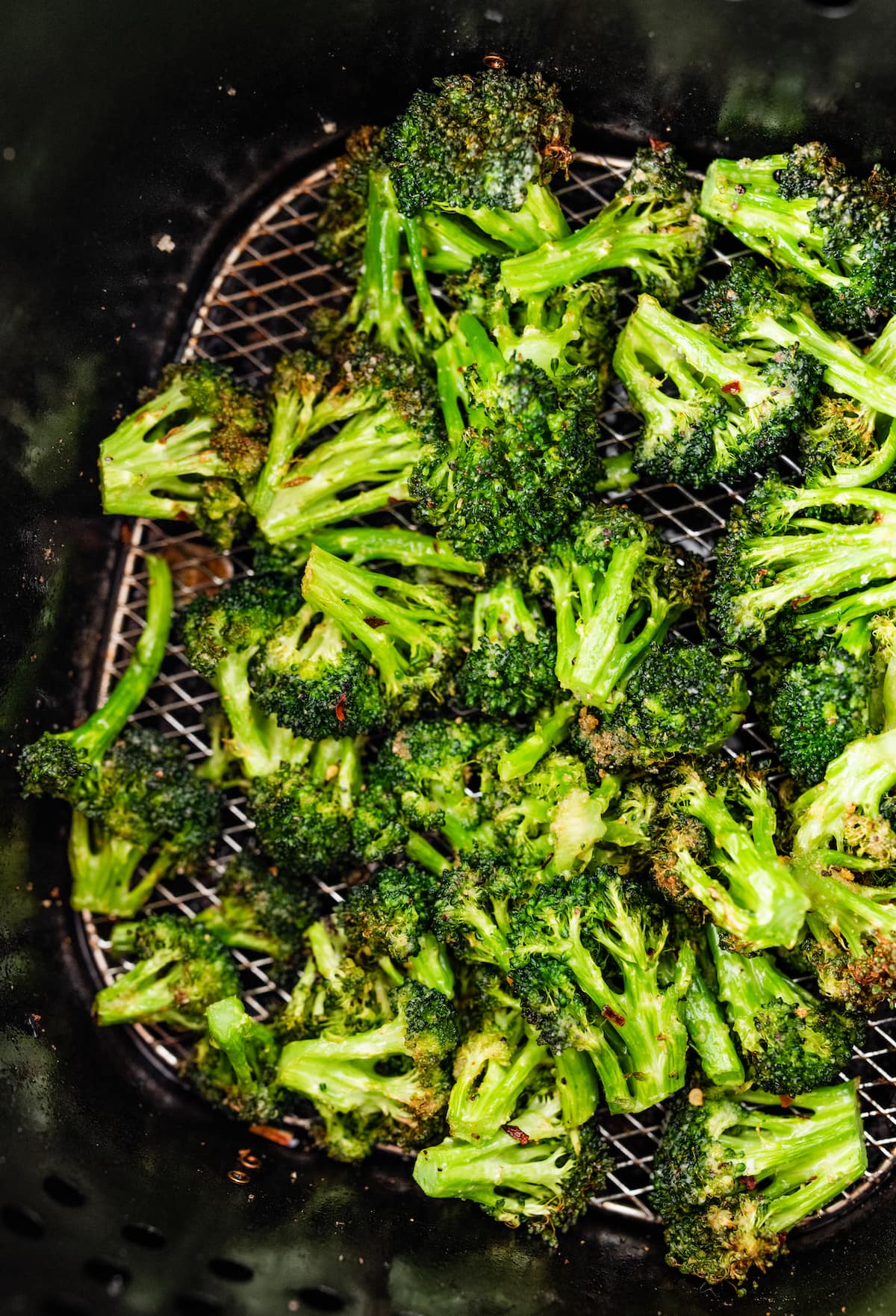 Seasoned air-fried broccoli in an air fryer basket.