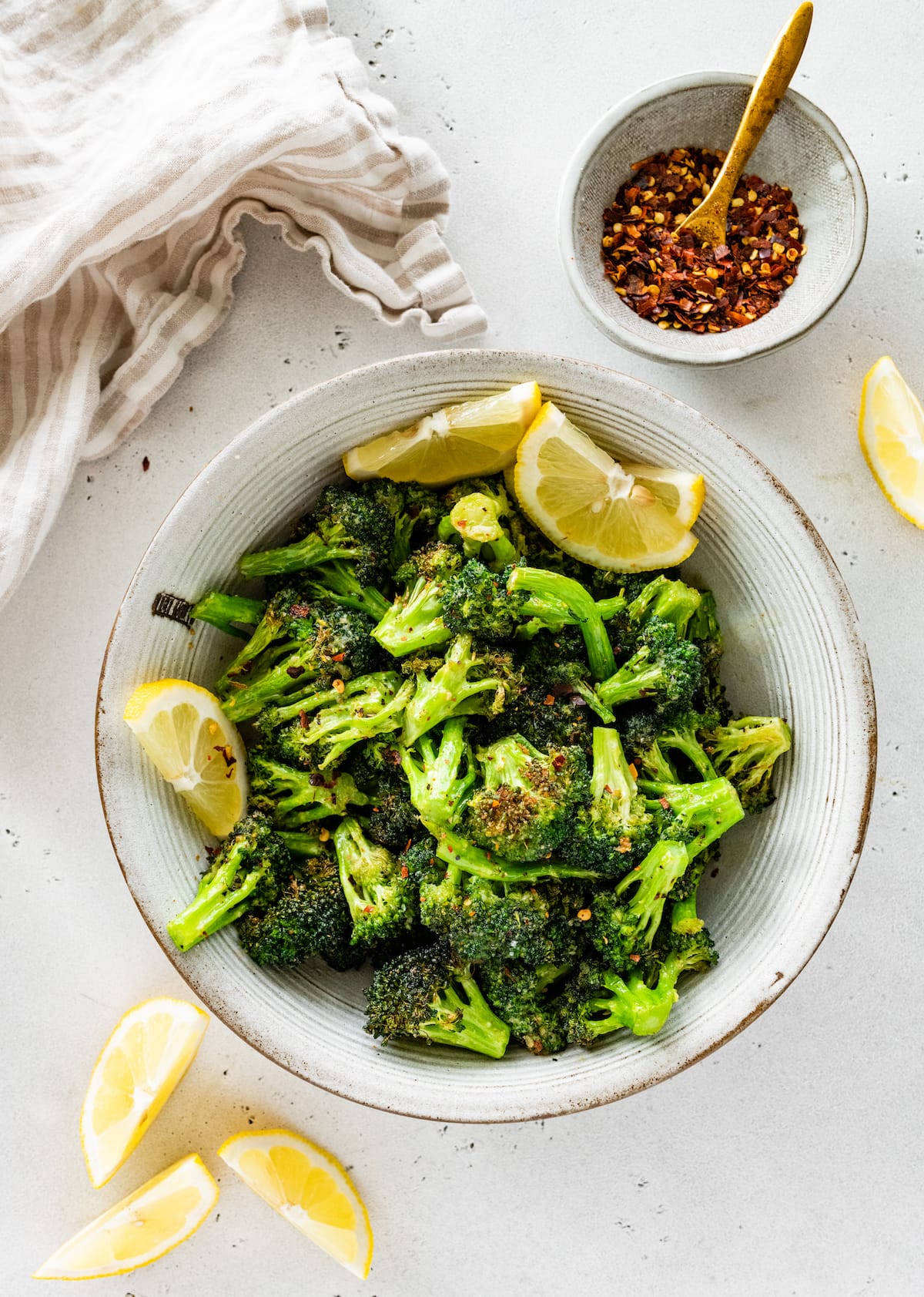 Seasoned air-fried broccoli in a large bowl with lemon wedges.