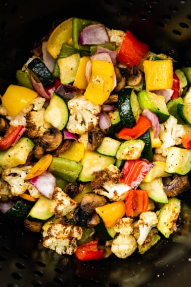 Air-fried vegetables in an air fryer. Vegetables include cauliflower, mushroom, onion, zucchini, and bell peppers.