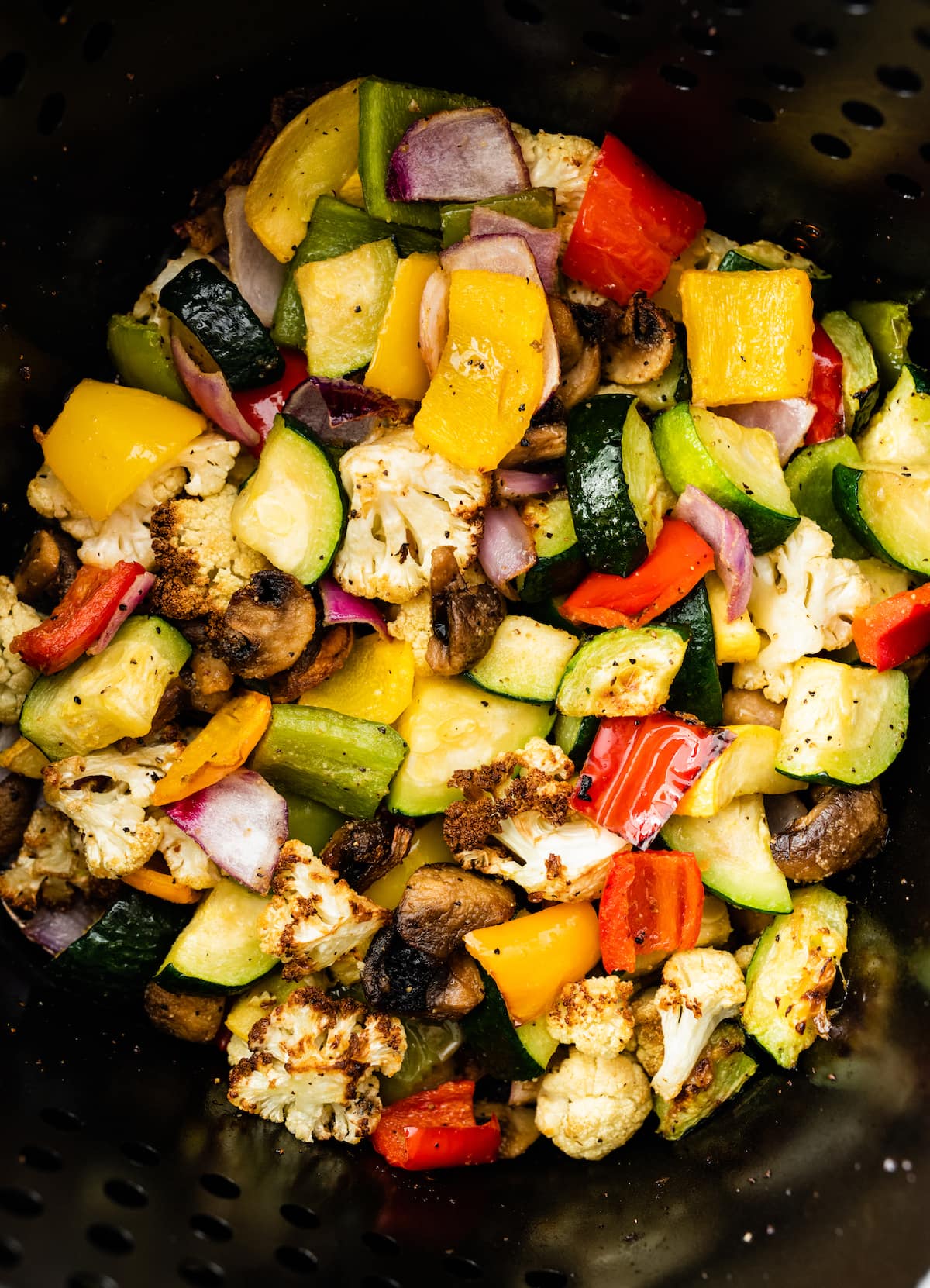 Air-fried vegetables in an air fryer. Vegetables include cauliflower, mushroom, onion, zucchini, and bell peppers.