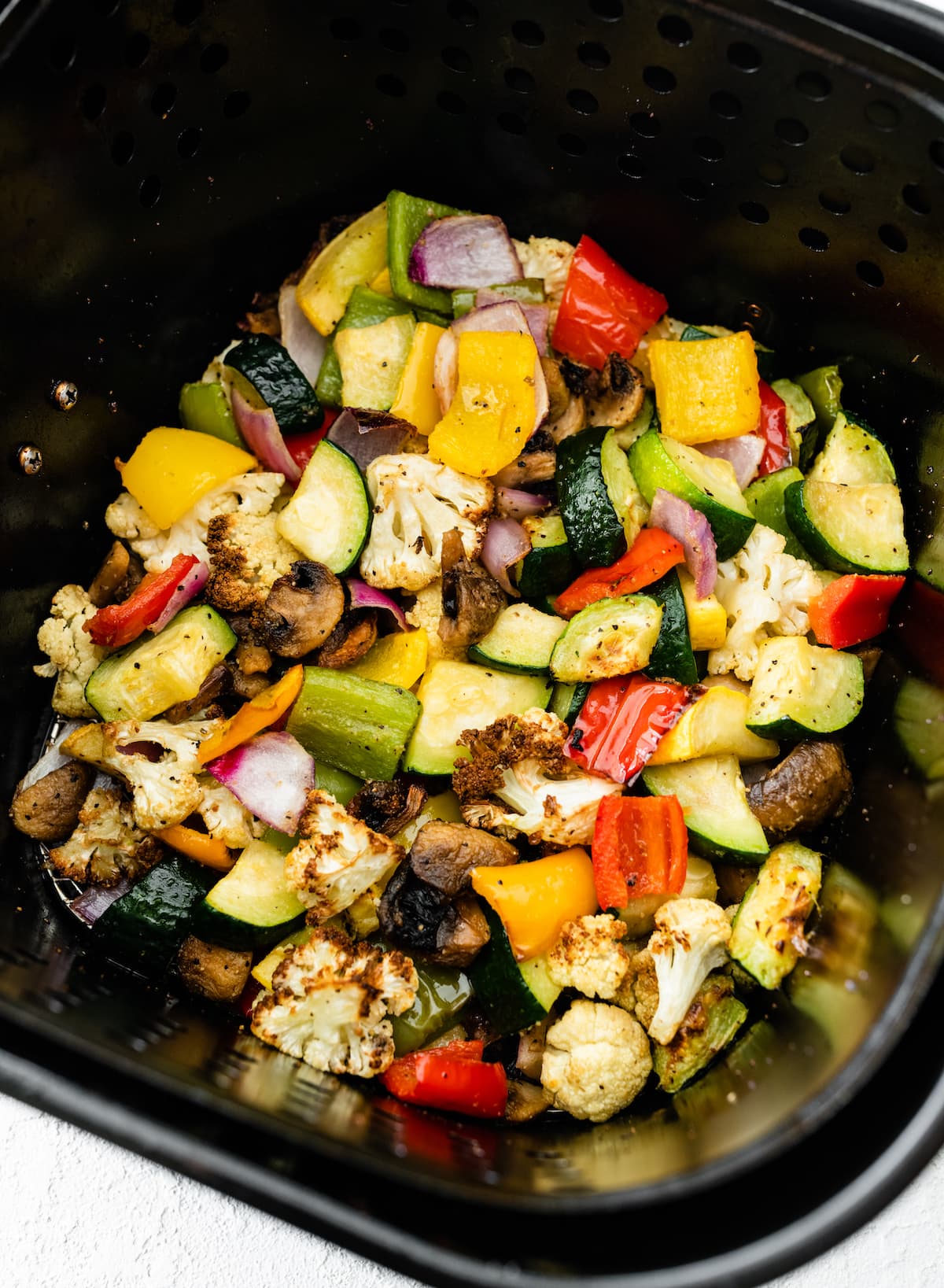 Air-fried vegetables in an air fryer. Vegetables include cauliflower, mushroom, onion, zucchini, and bell peppers.