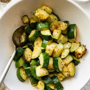Air-fried zucchini in a bowl with a metal spoon.