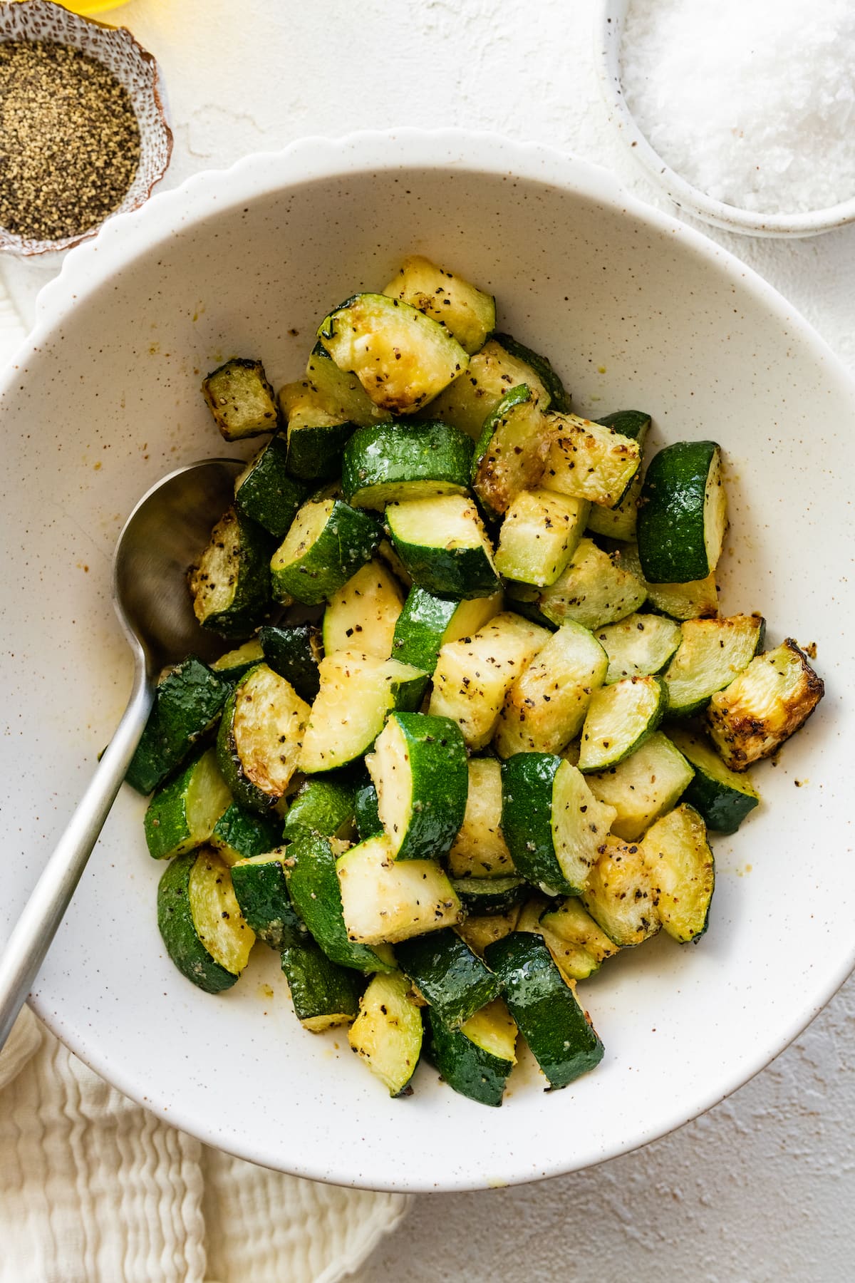 Air-fried zucchini in a bowl with a metal spoon.