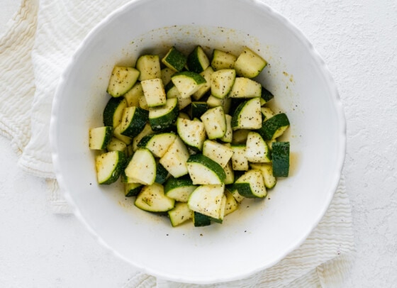 Chopped zucchini in a white bowl with seasonings added.