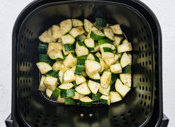 Seasoned chopped zucchini in an air fryer basket before being air-fried.