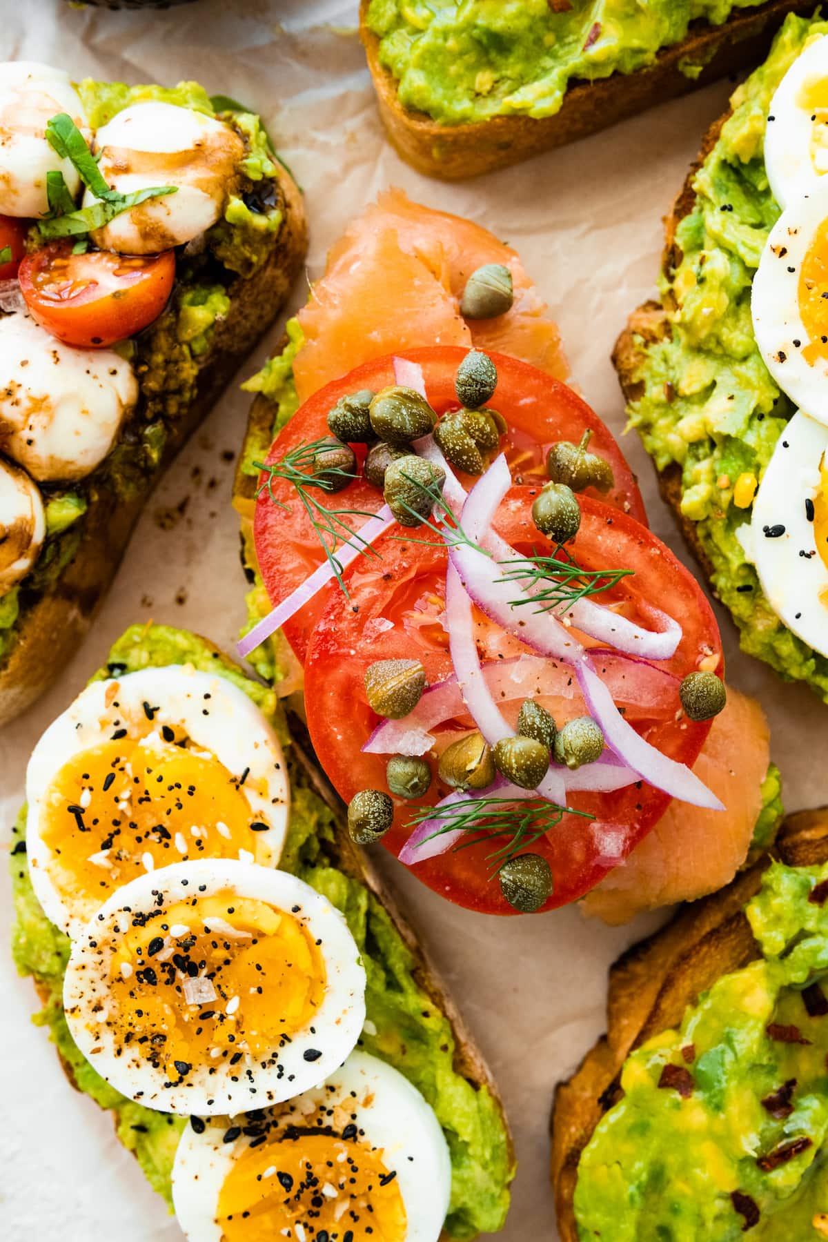 Four variations of avocado toast on parchment paper.