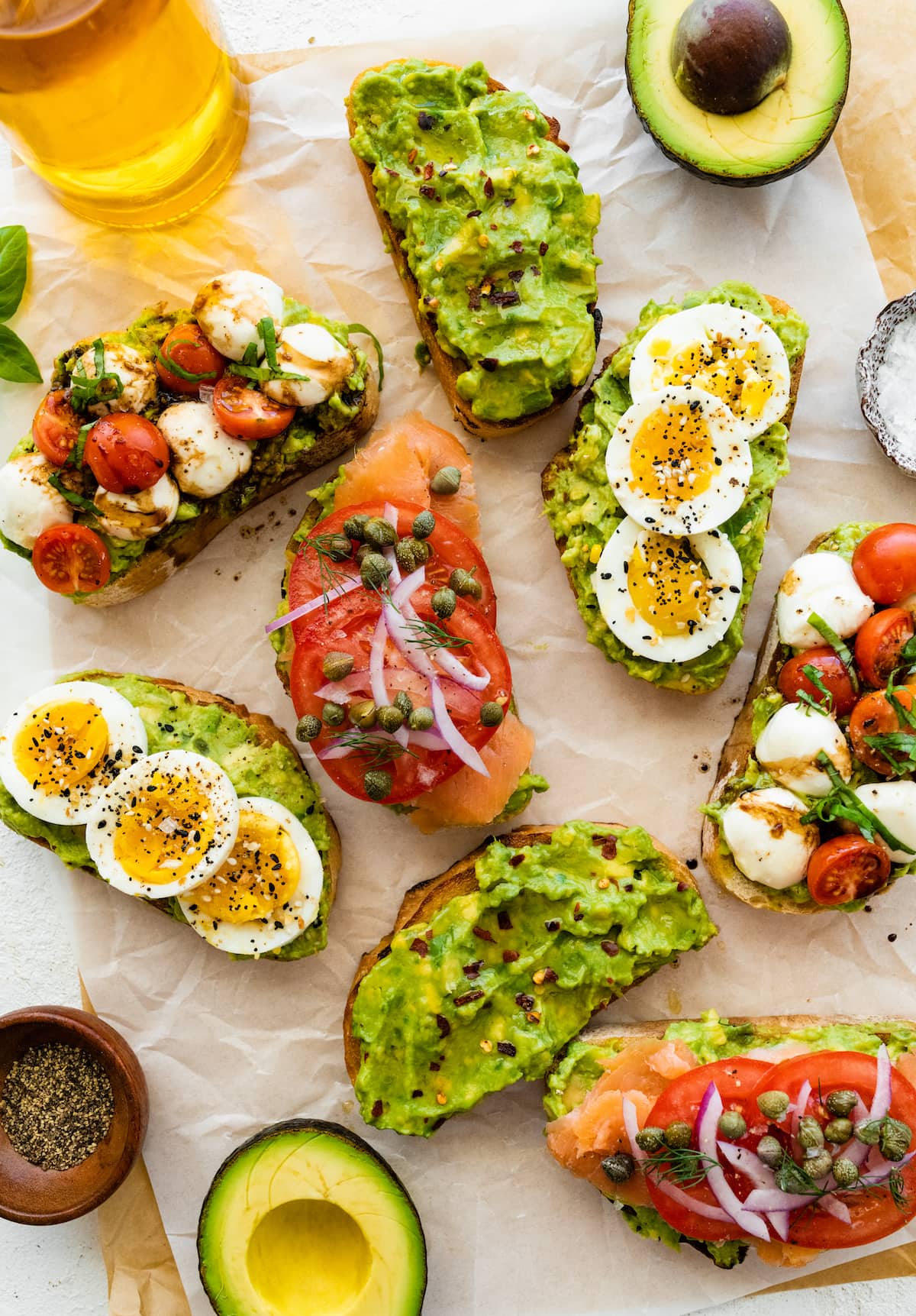 Four variations of avocado toast on parchment paper.