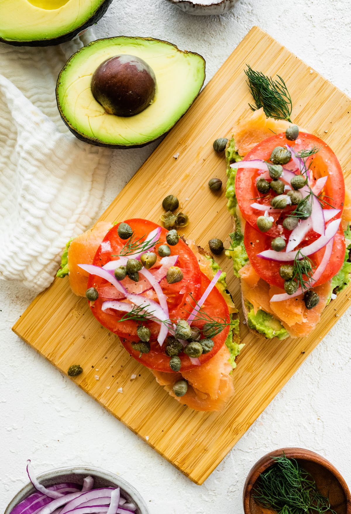 Smoked salmon avocado toast on a wooden cutting board.