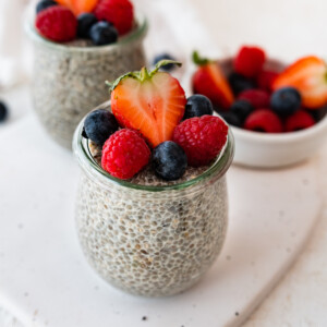 Two glass cups with chia pudding on a table topped with fresh berries.