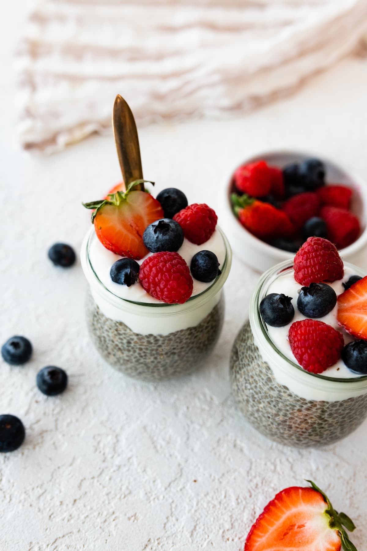 Two glass cups with chia pudding on a table topped with yogurt and fresh berries.