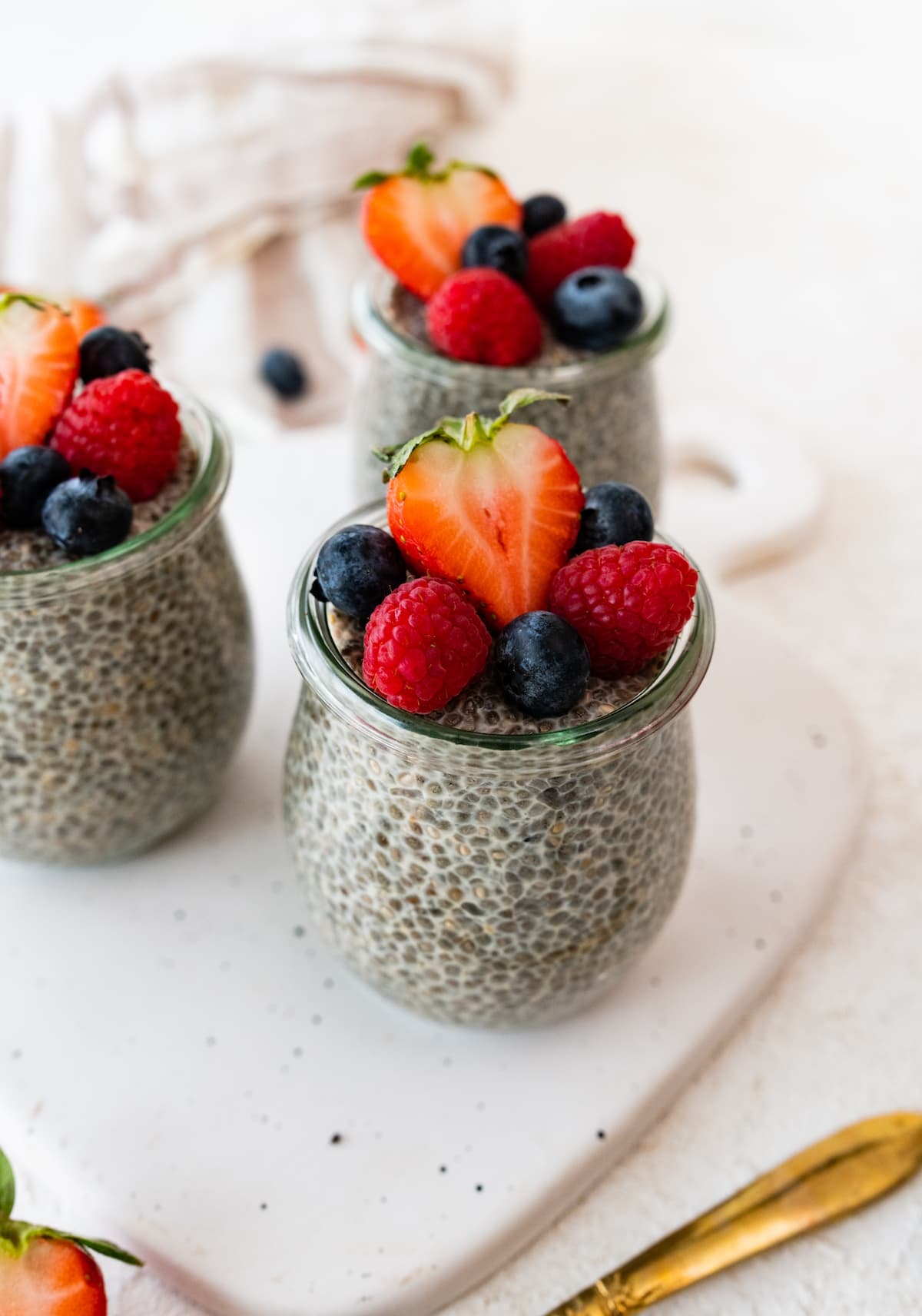 Three glass cups of chia pudding on a cutting board, topped with fresh berries.