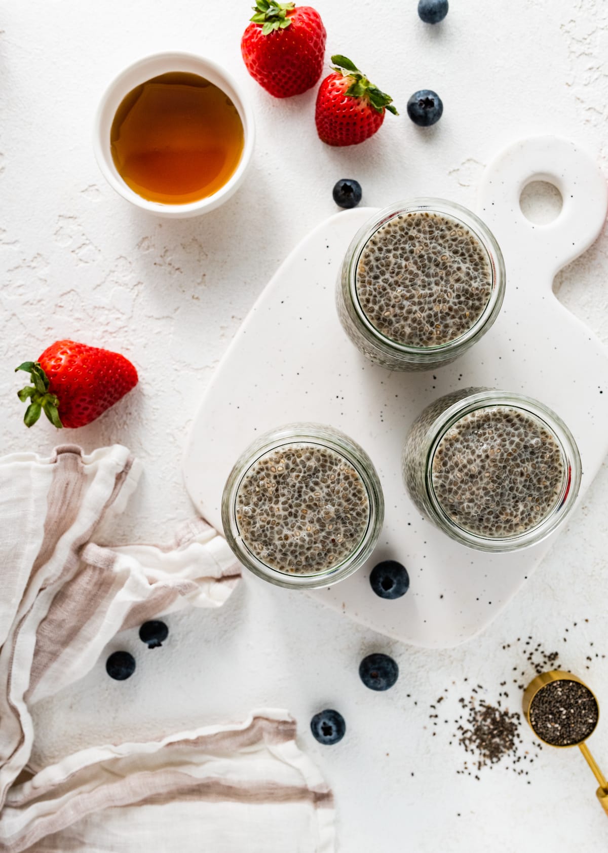 Three glass cups with chia pudding on a cutting board.