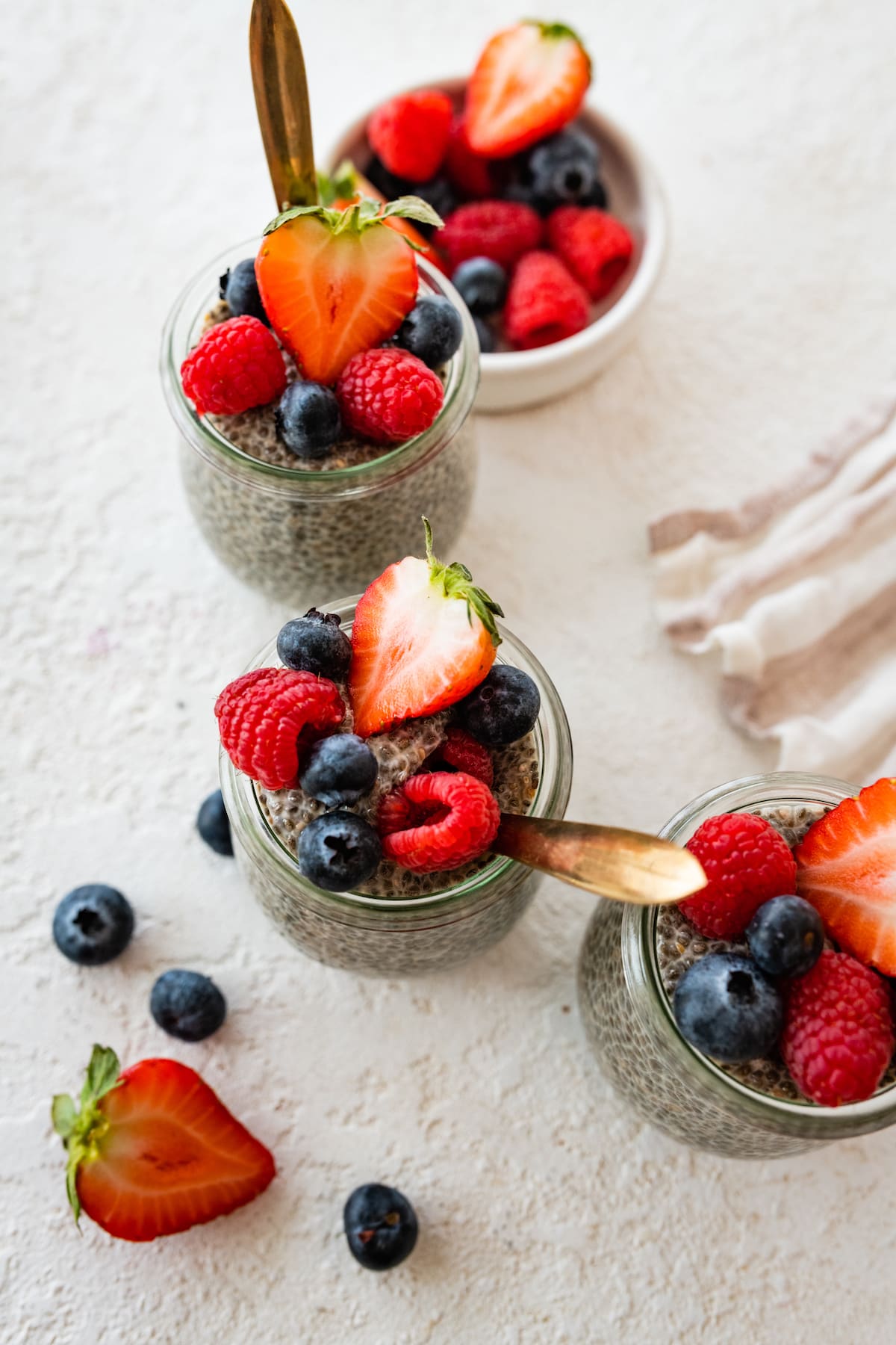 Three glass cups of chia pudding topped with fresh berries.